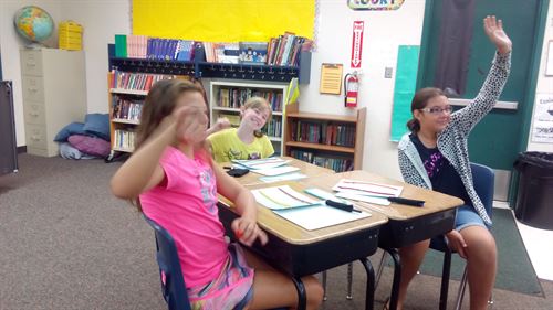 Students sitting at a table, one is raising her hand